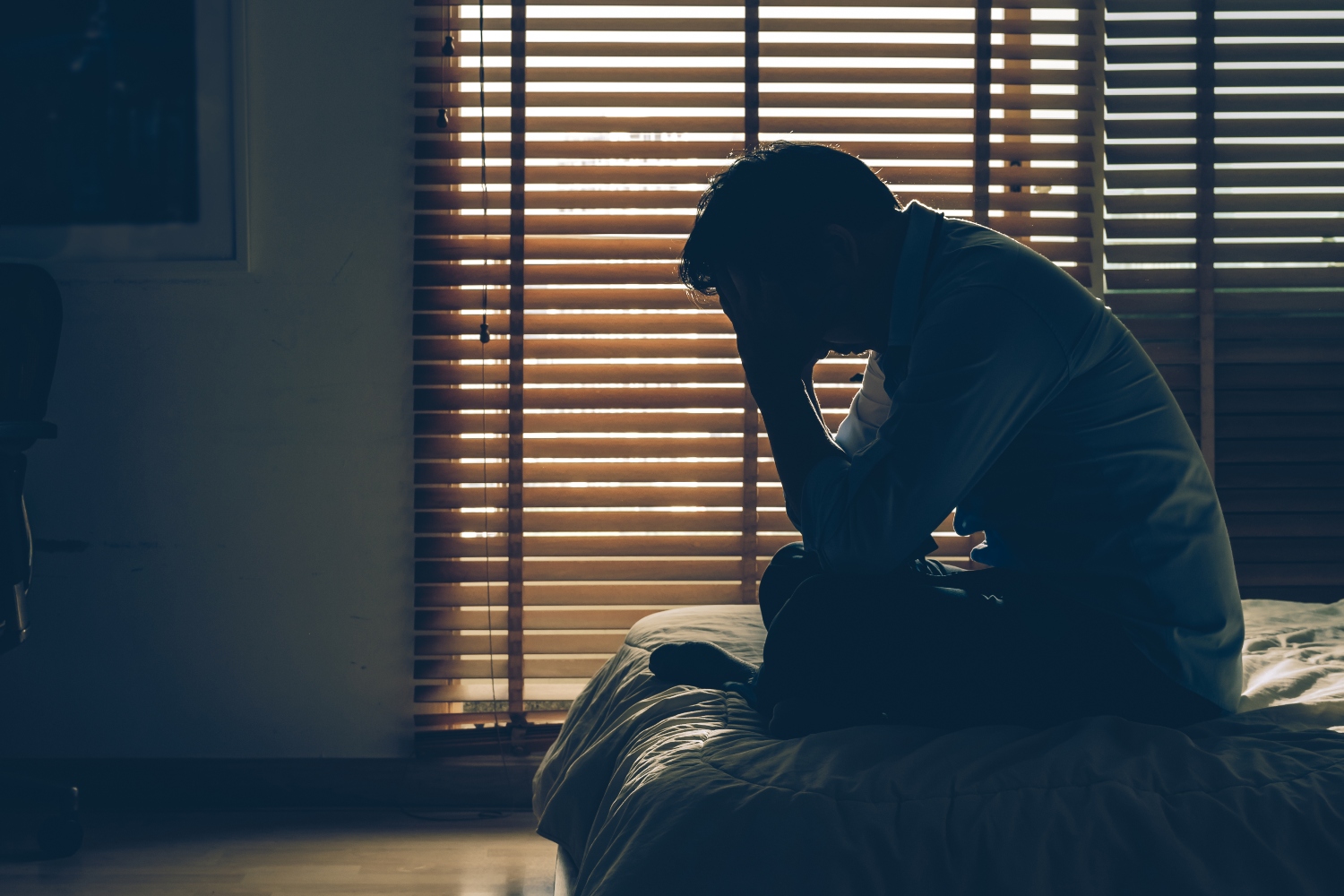 Sad businessman sitting head in hands on the bed in the dark bedroom with low light environment, dramatic concept, vintage tone color