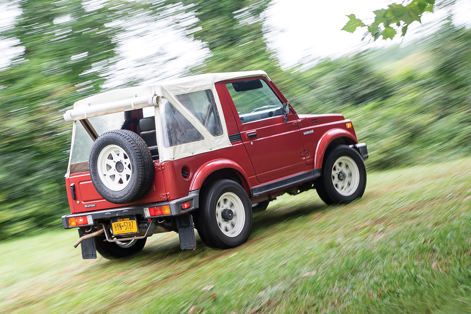 A 1986 Suzuki Samurai SUV driving down a dirt path. The old-school sport utility vehicle is on Hagerty's 2022 Bull Market List.