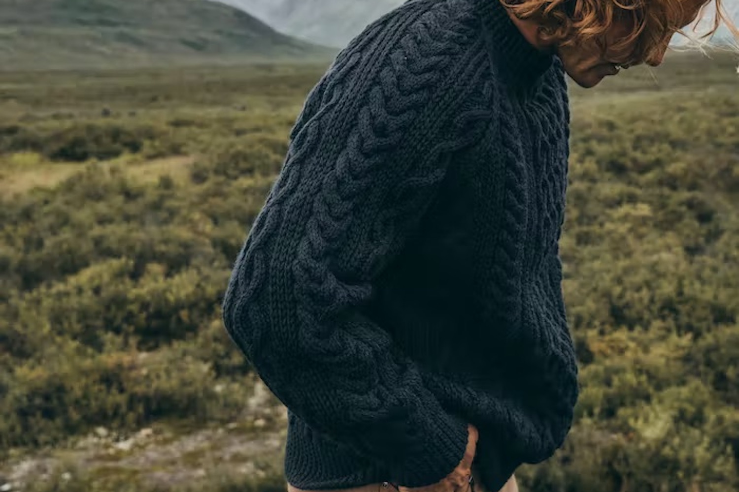 a model in a navy Filson fisherman sweater in a grassy field