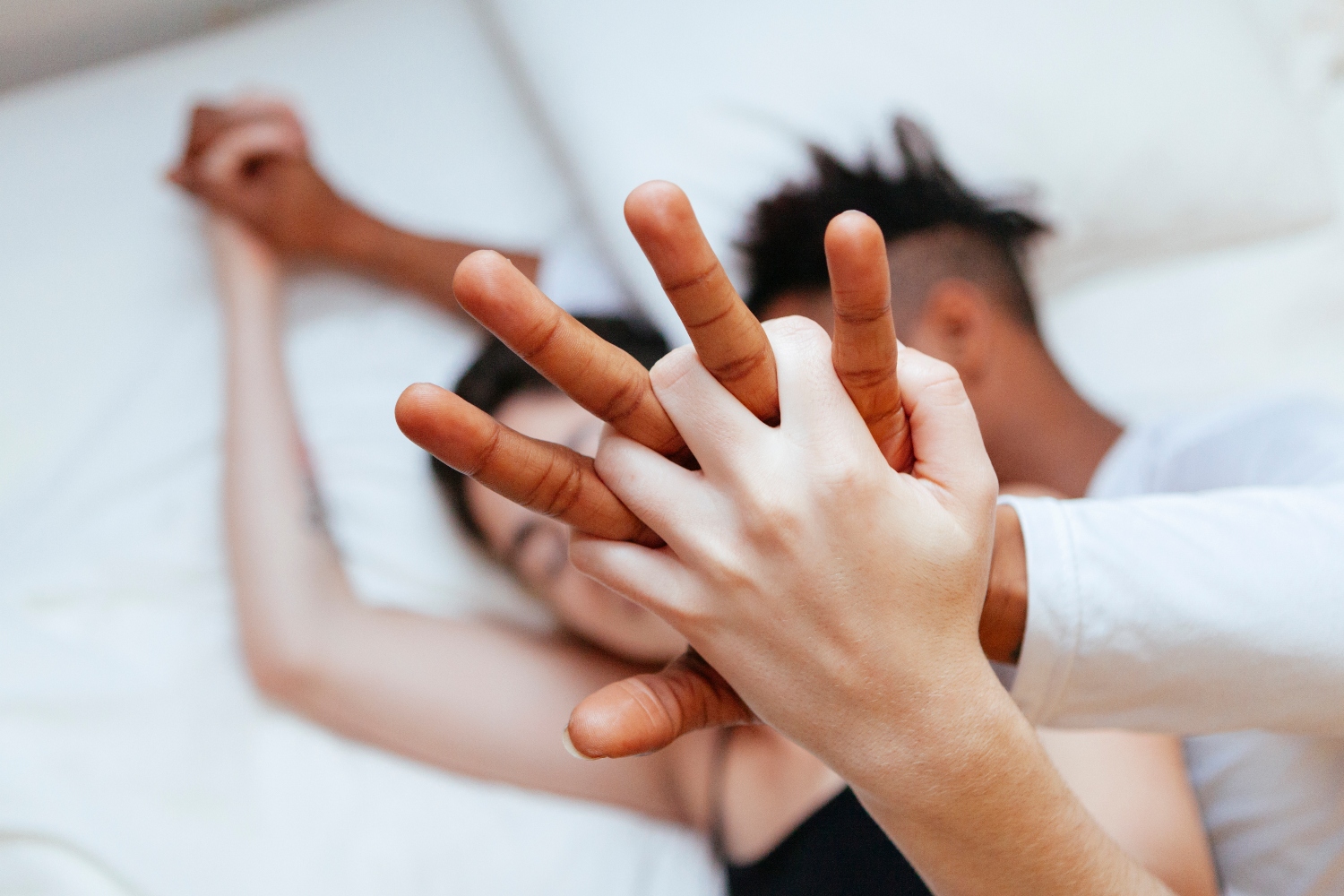 Interracial heterosexual couple holding hands at home. Millennial young love between two different races. Couple on an intimate moment lying on a bed. Lifestyle at home. Young people.