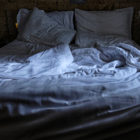 Rumpled sheets on an empty bed in a dark room