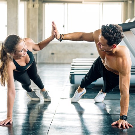 Happy sporty couple giving high five to each other while doing push up or side plank exercise together in gym