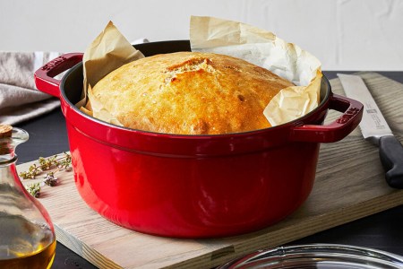 A red cocotte from Staub with a loaf of bread inside. The four-quart Dutch oven with a glass lid is on sale at Sur La Table for December 2021.