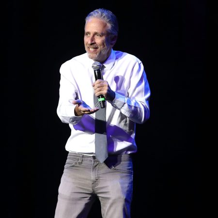 Jon Stewart in a white shirt and tie speaking into a microphone at the 10th Annual Stand Up For Heroes - Show at The Theater at Madison Square Garden on November 1, 2016 in New York City