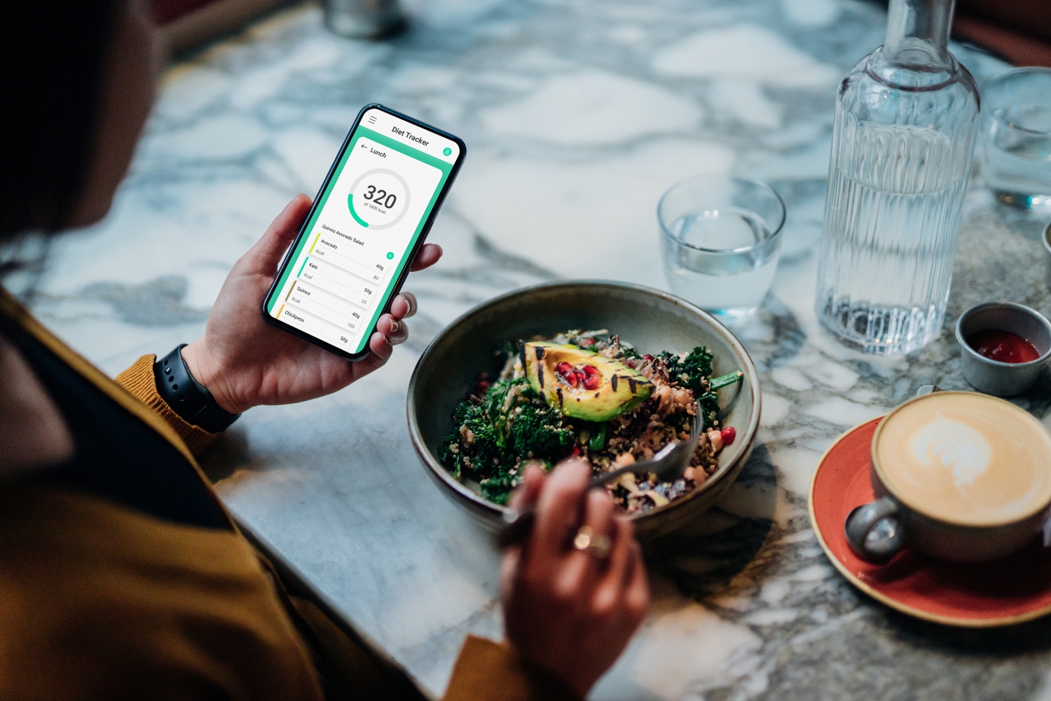 Over the shoulder shot of young Asian woman checking calories intake and nutrition values using diet tracking app on smart phone while eating avocado and quinoa salad at the cafe. Healthy eating lifestyles.