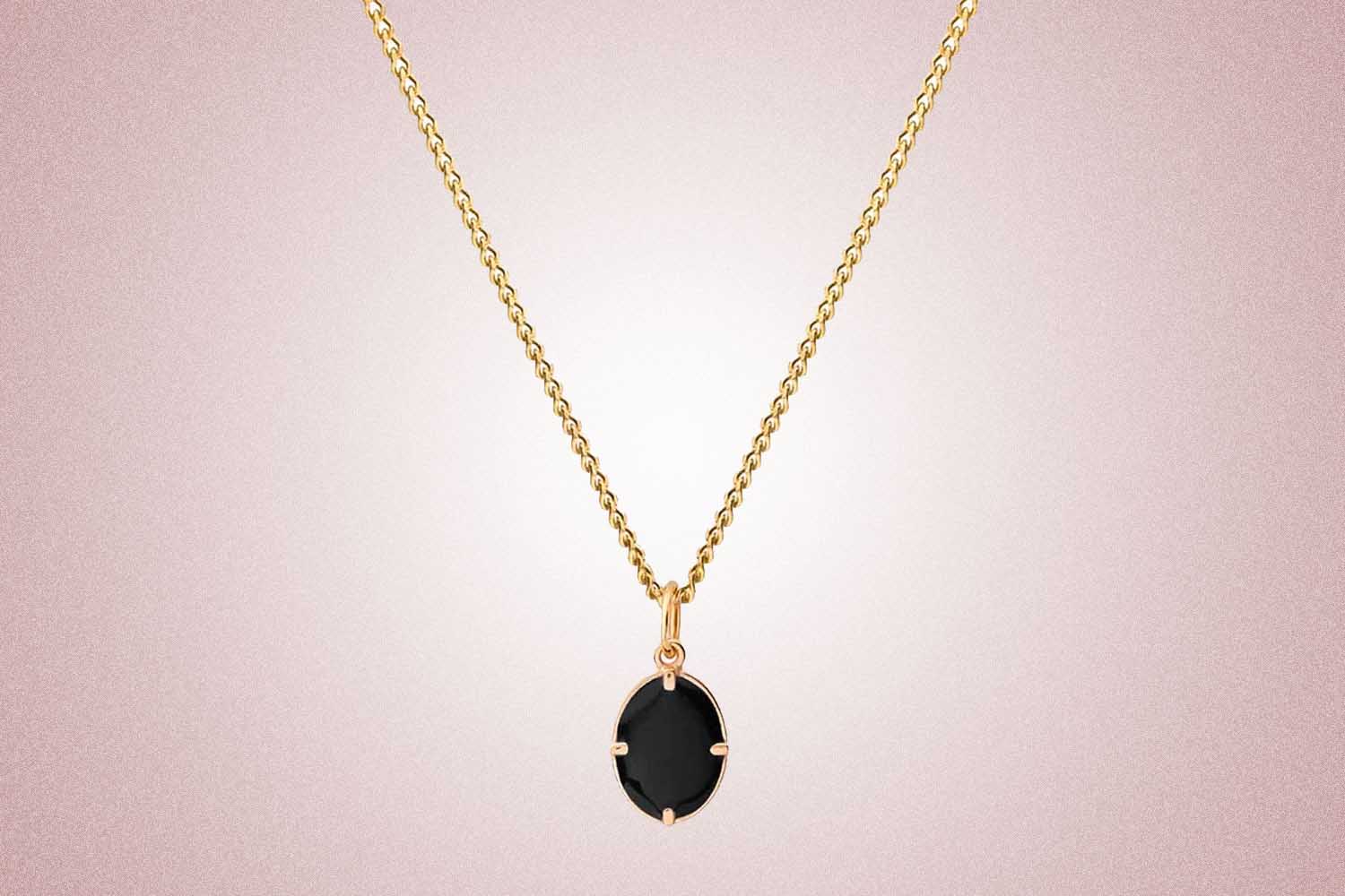 A gold necklace with a black enamel stone, a perfect valentine's day gift, on a pink background.