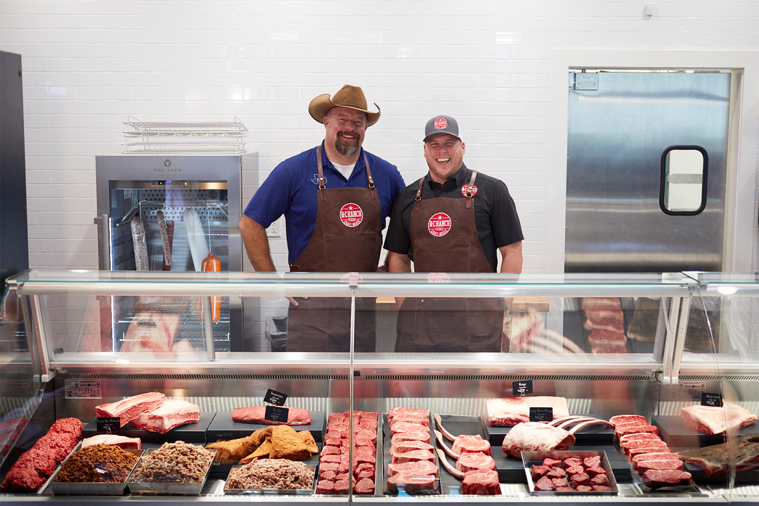 Blake Robertson and Ryan Cade of R-C Ranch standing behind their butcher shop's case of Wagyu beef