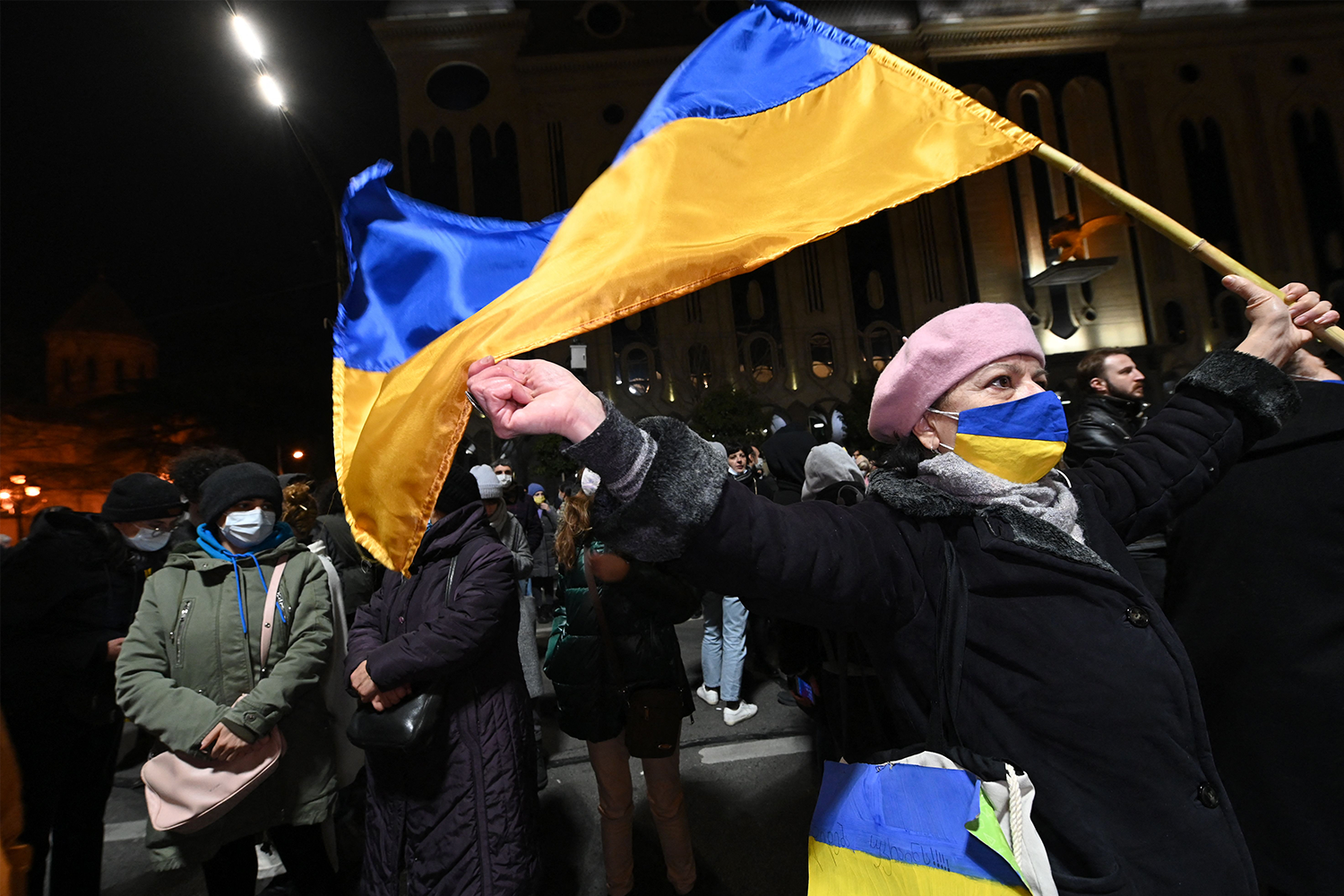 A woman wearing a face mask with the colors of the Ukrainian flag and waving a flag of Ukraine