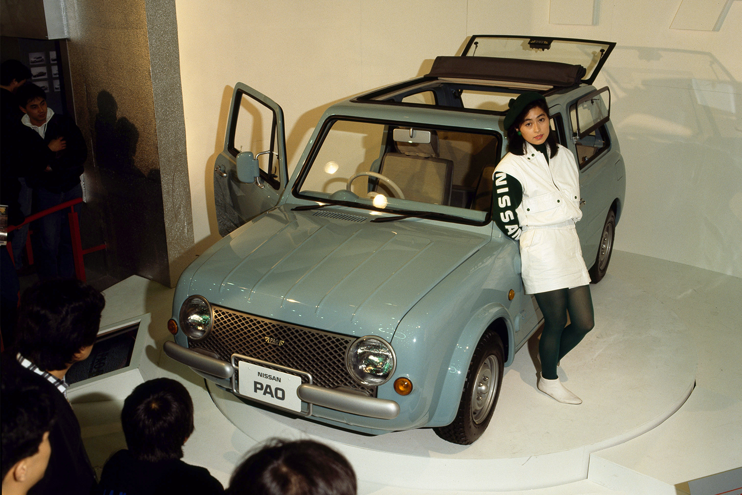 A woman standing next to the Nissan Pao, one of the Japanese brand's Pike Factory cars, at an auto show