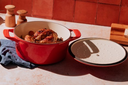 A red Dutch oven from the brand Made In sitting on a table with a chicken in the pot. We reviewed the enameled cast-iron Dutch oven and compared it to Staub and Le Creuset.