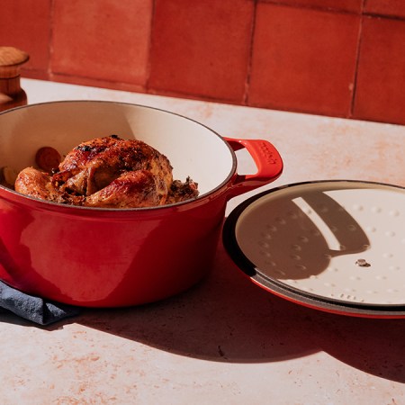 A red Dutch oven from the brand Made In sitting on a table with a chicken in the pot. We reviewed the enameled cast-iron Dutch oven and compared it to Staub and Le Creuset.