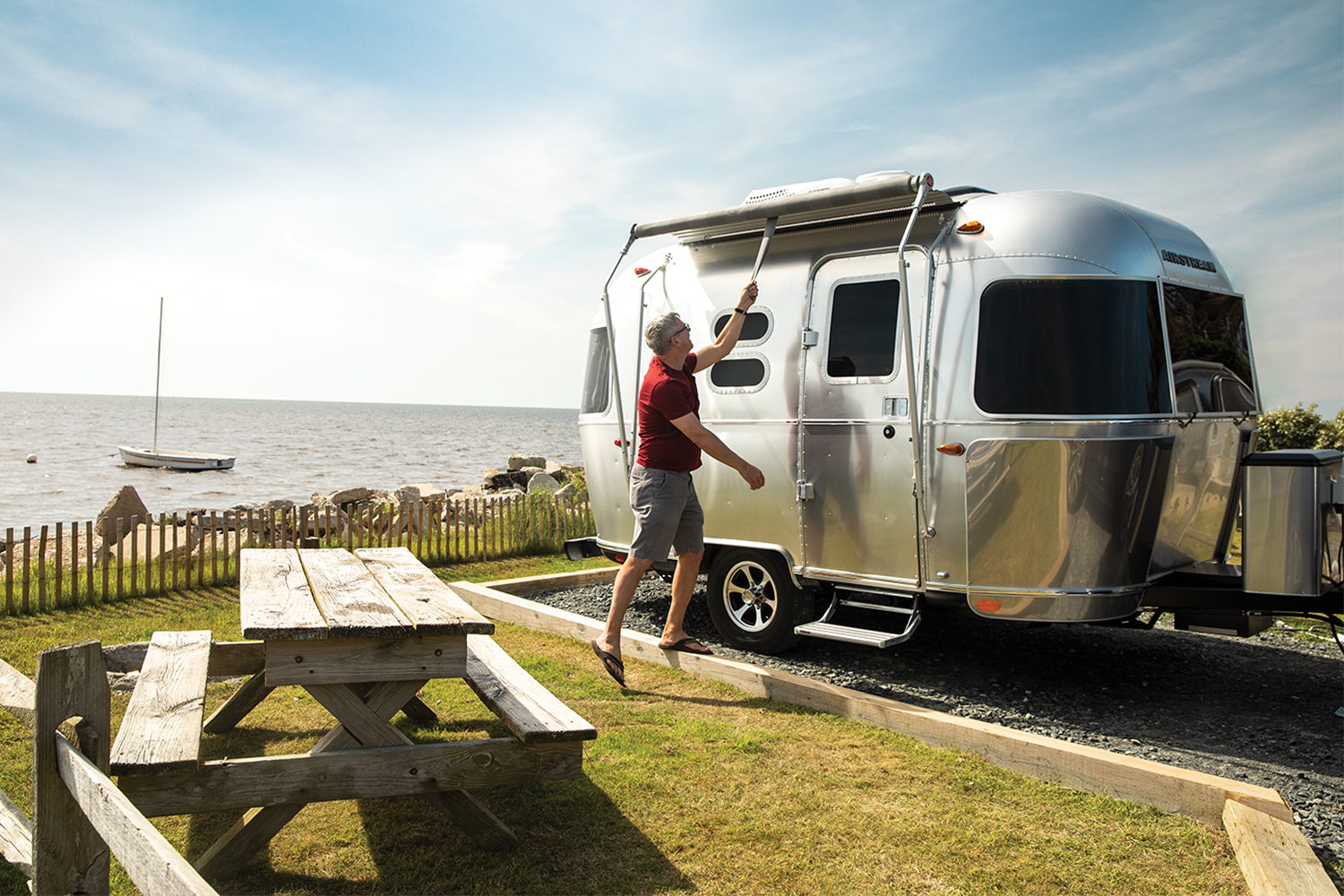 A man setting up his aluminum Airstream travel trailer next to a picnic table overlooking the ocean. According to new financial results, RV backlogs are still growing two years into the pandemic.