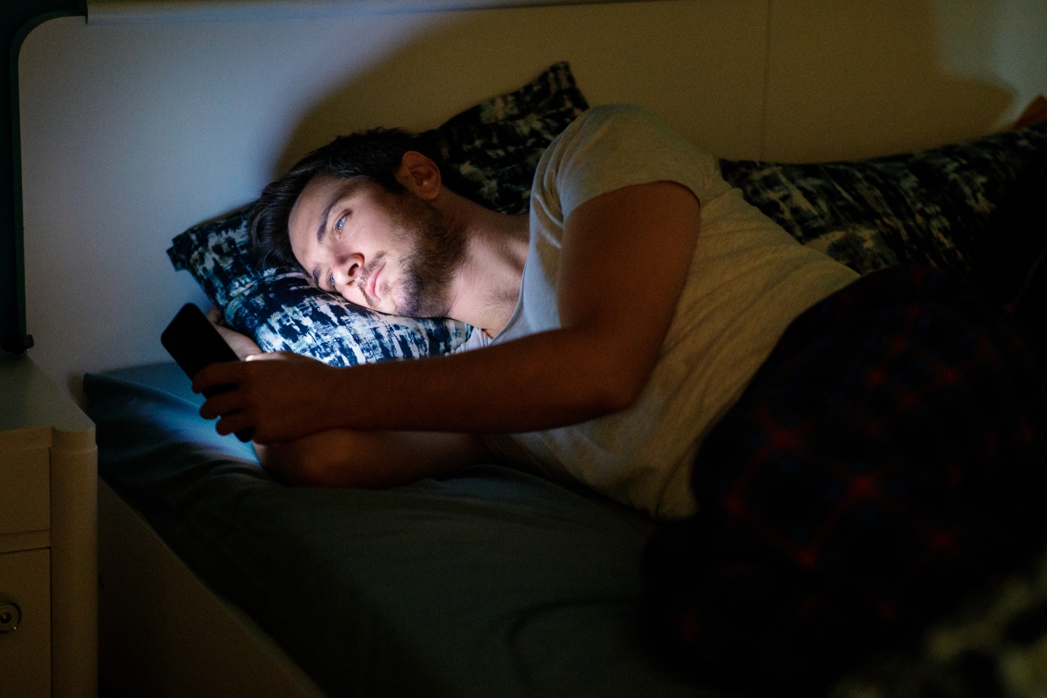 Young man lying in bed at night and using his smart phone