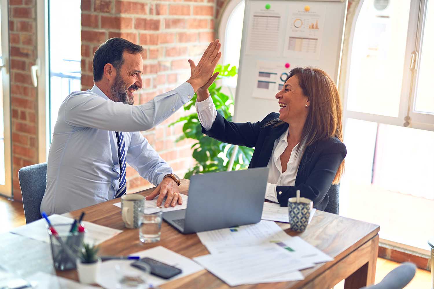 A man and woman high five at a desk.