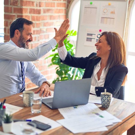 A man and woman high five at a desk.