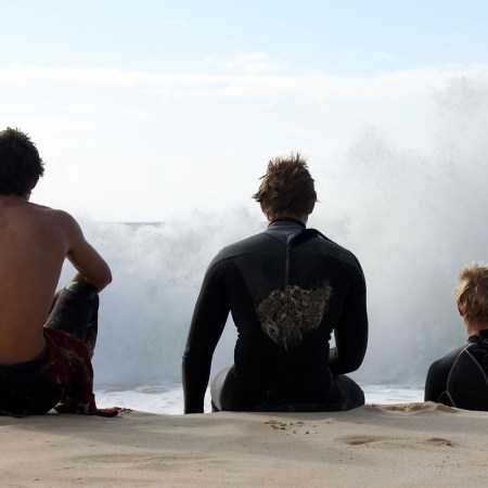 Three men sitting together on a beach.