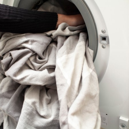 Close-up of hands loading bed sheets into a washing machine