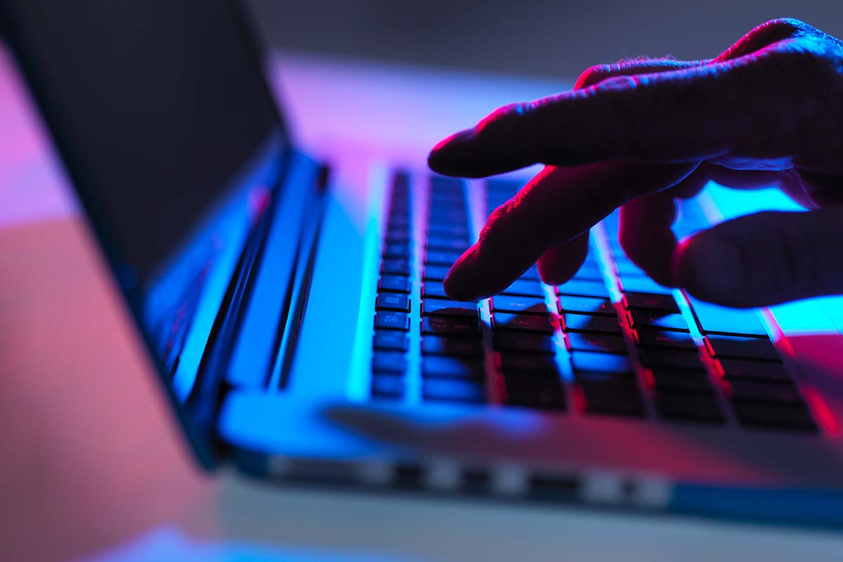 Silhouette of male hand typing on laptop keyboard at night - stock photo