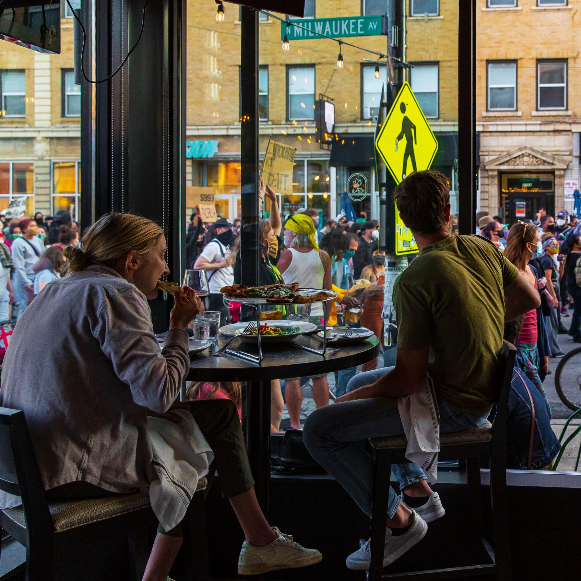 A couple eating brunch while protesters march by in Chicago, as photographed by Vashon Jordan Jr.