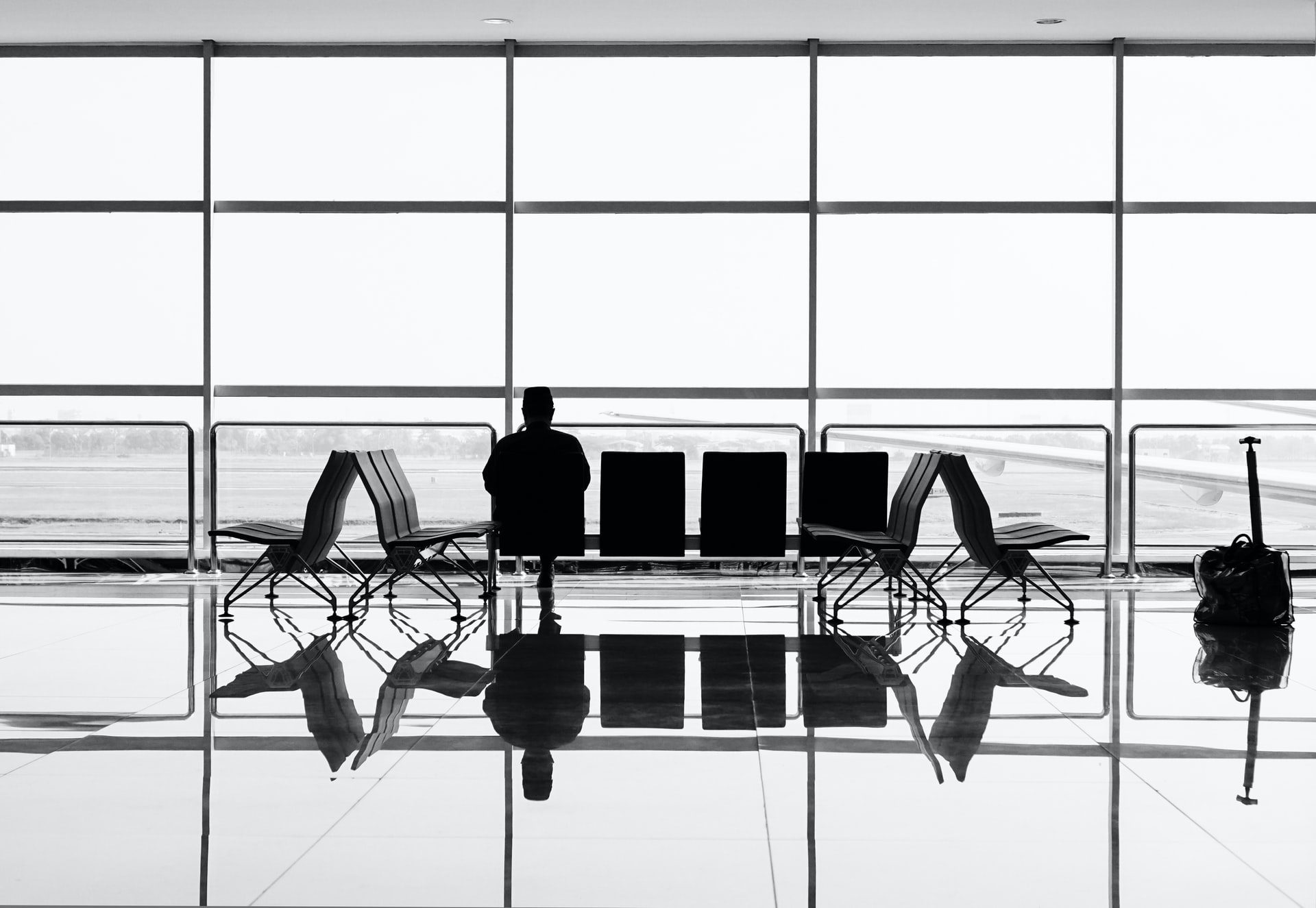 A black and white photo of a person sitting alone in an airport terminal looking out the window