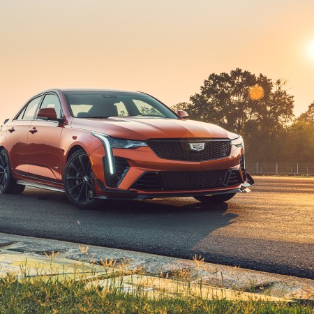 The Cadillac CT4-V Blackwing in orange sitting on a track with the sun setting in the background. We reviewed the 2022 V6 sport sedan and its sibling the CT5-V Blackwing.