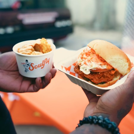 A fried chicken sandwich and sides from Soulfly Chicken being held in two hands