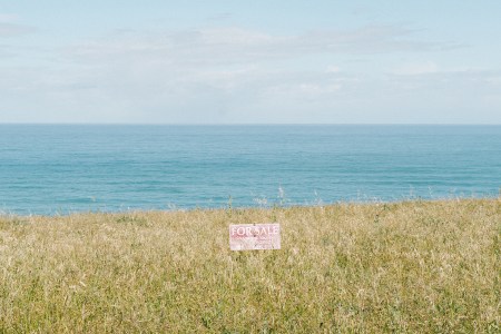 Lot for Sale sign in a field with water behind it