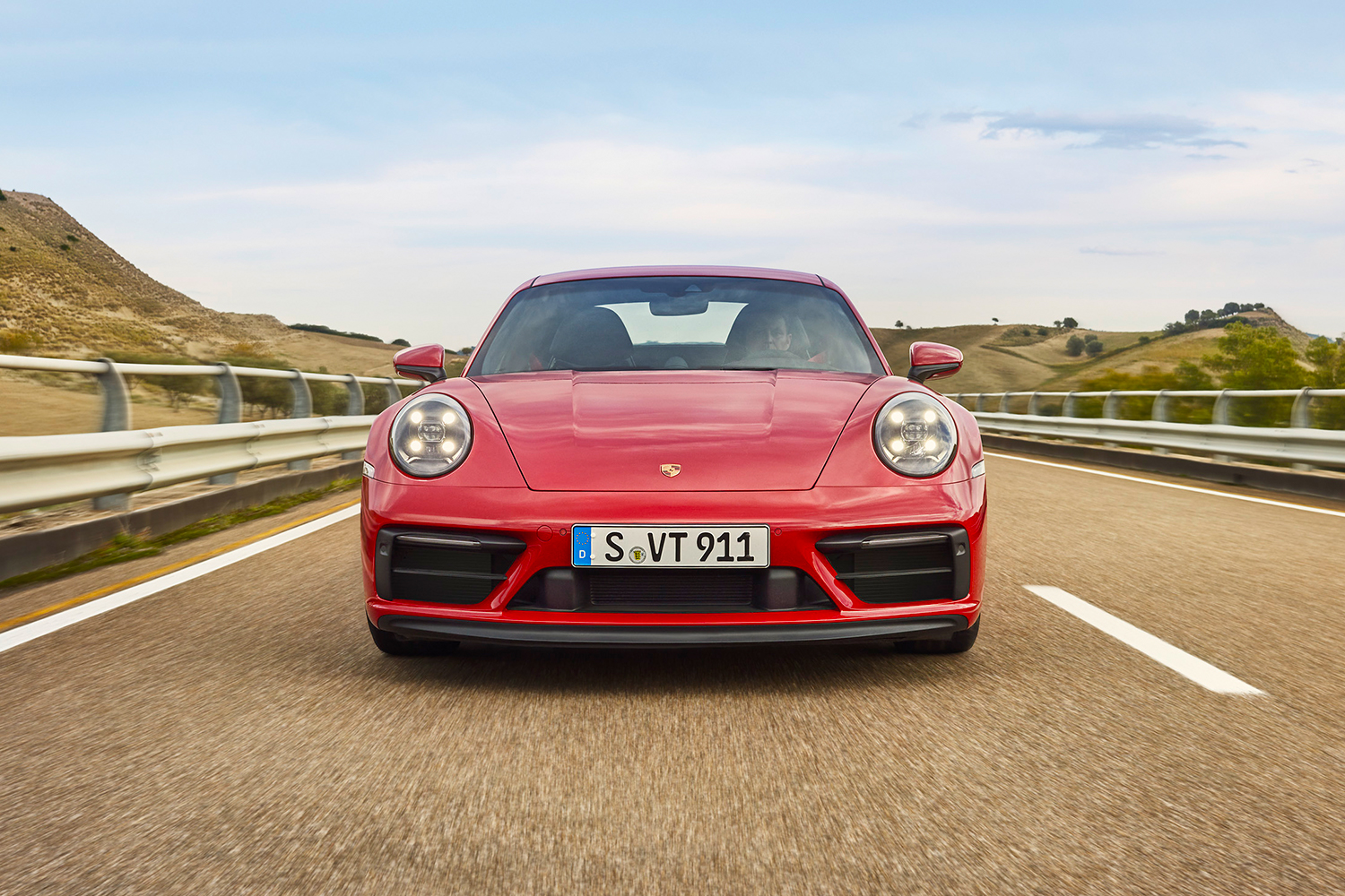 A straight front-end shot of a red 2022 Porsche 911 Carrera GTS sports car driving down the road