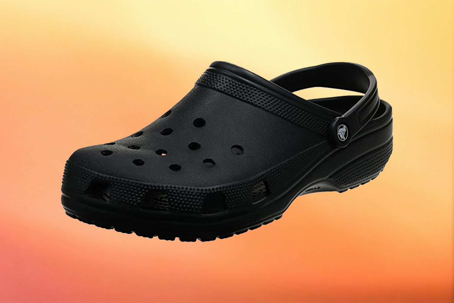 A singular black Croc clog on a yellow-orange gradient background