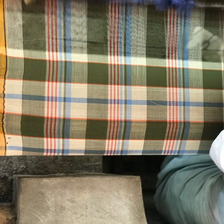 A green, red and beige madras pattern being made by an artisan