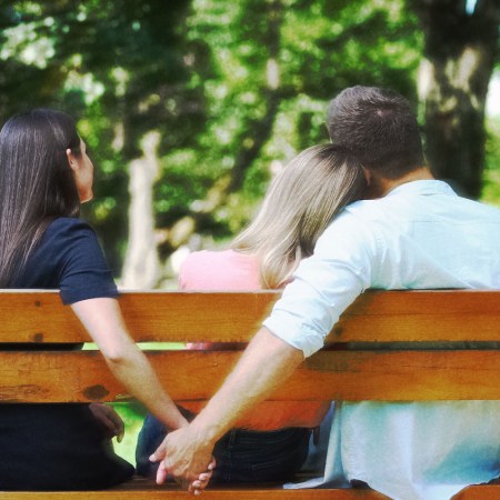 Three people sitting on a bench, one woman has her head resting on a man's shoulder, while the man hold hands with another woman.