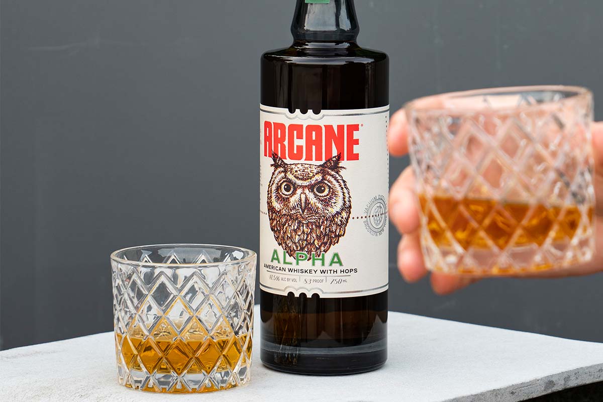 A bottle of Arcane Alpha and two glasses of whiskey on a table