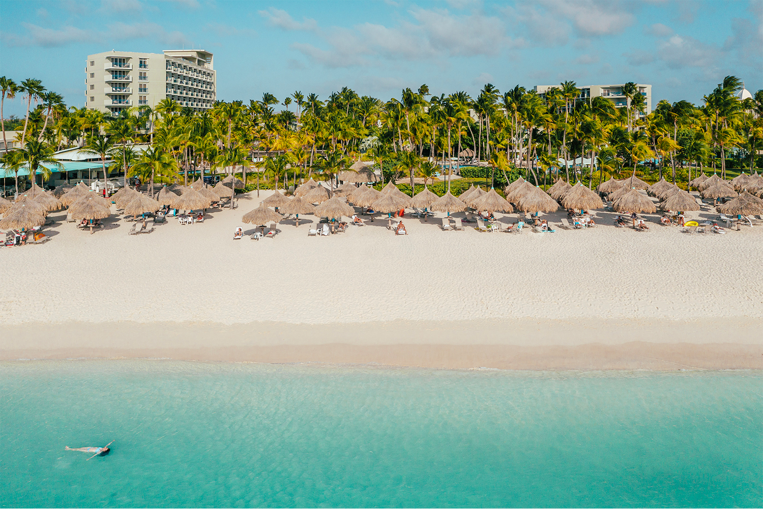 A person floating in the ocean off the beach of the Hilton Aruba hotel and resort