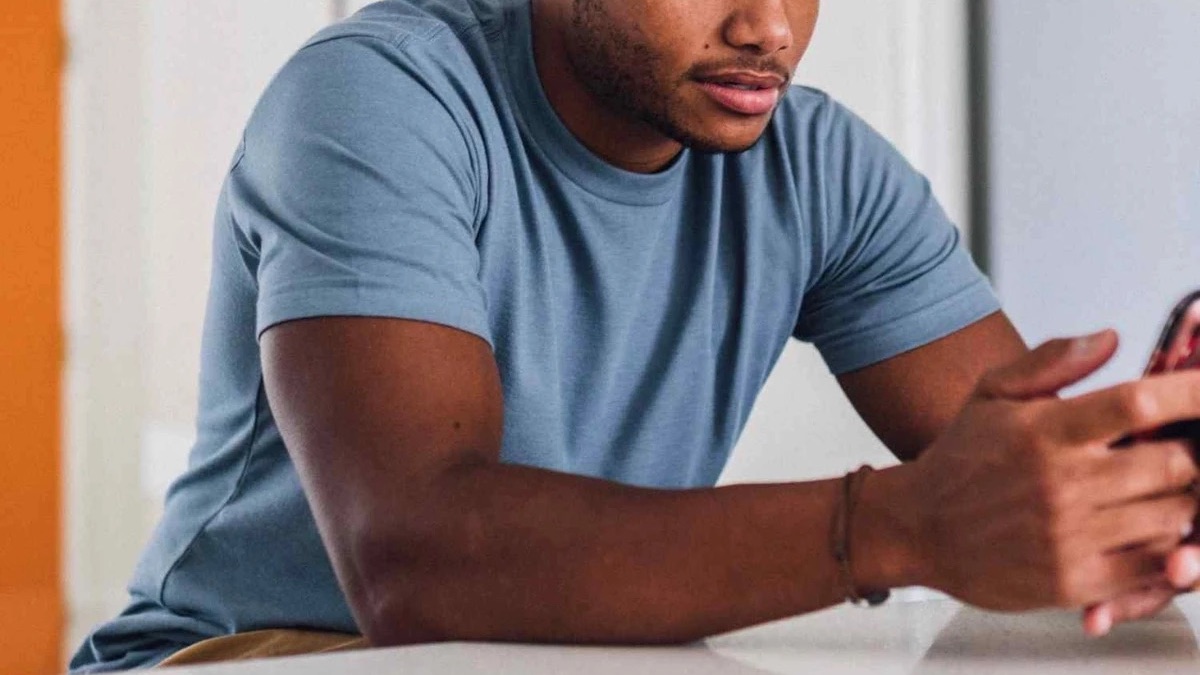 a model in a blue Fresh Clean Threads Tee resting and on his phone on a marble countertop