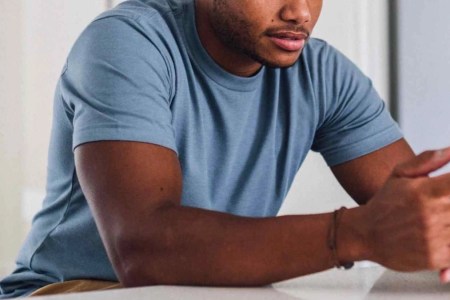 a model in a blue Fresh Clean Threads Tee resting and on his phone on a marble countertop