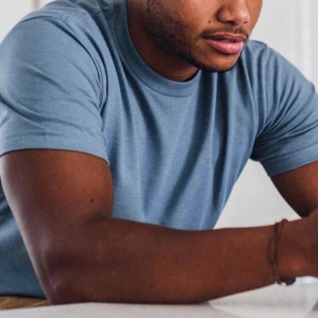 a model in a blue Fresh Clean Threads Tee resting and on his phone on a marble countertop