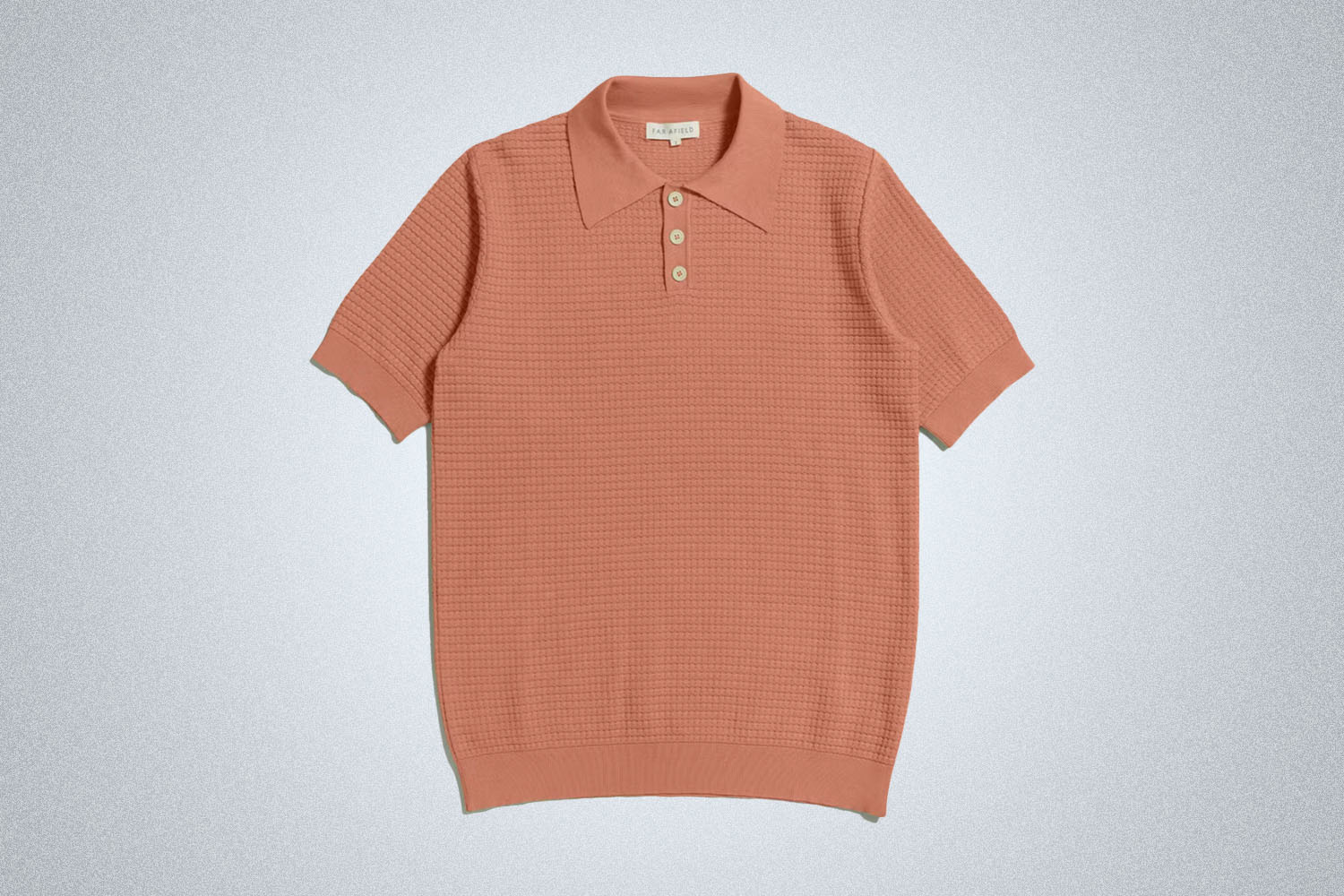 a rusty orange-colored knit polo shirt from Far Afield on a grey background