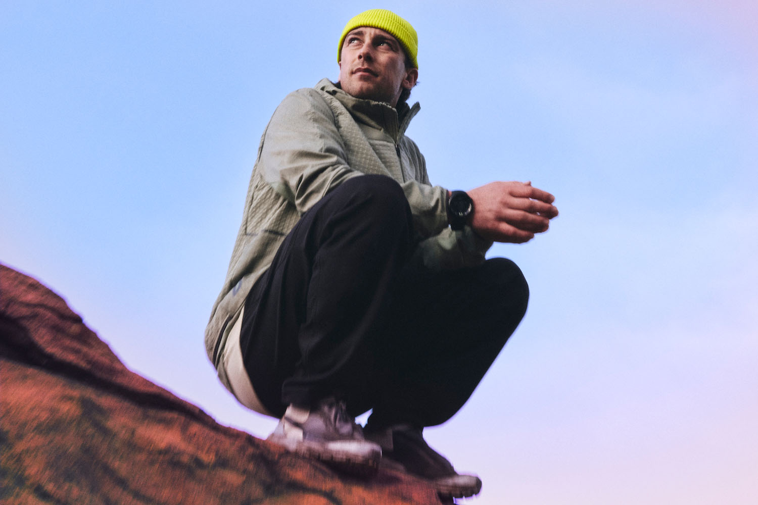 A model in Lululemon Hike clothing squatting on a rock against a blue sky