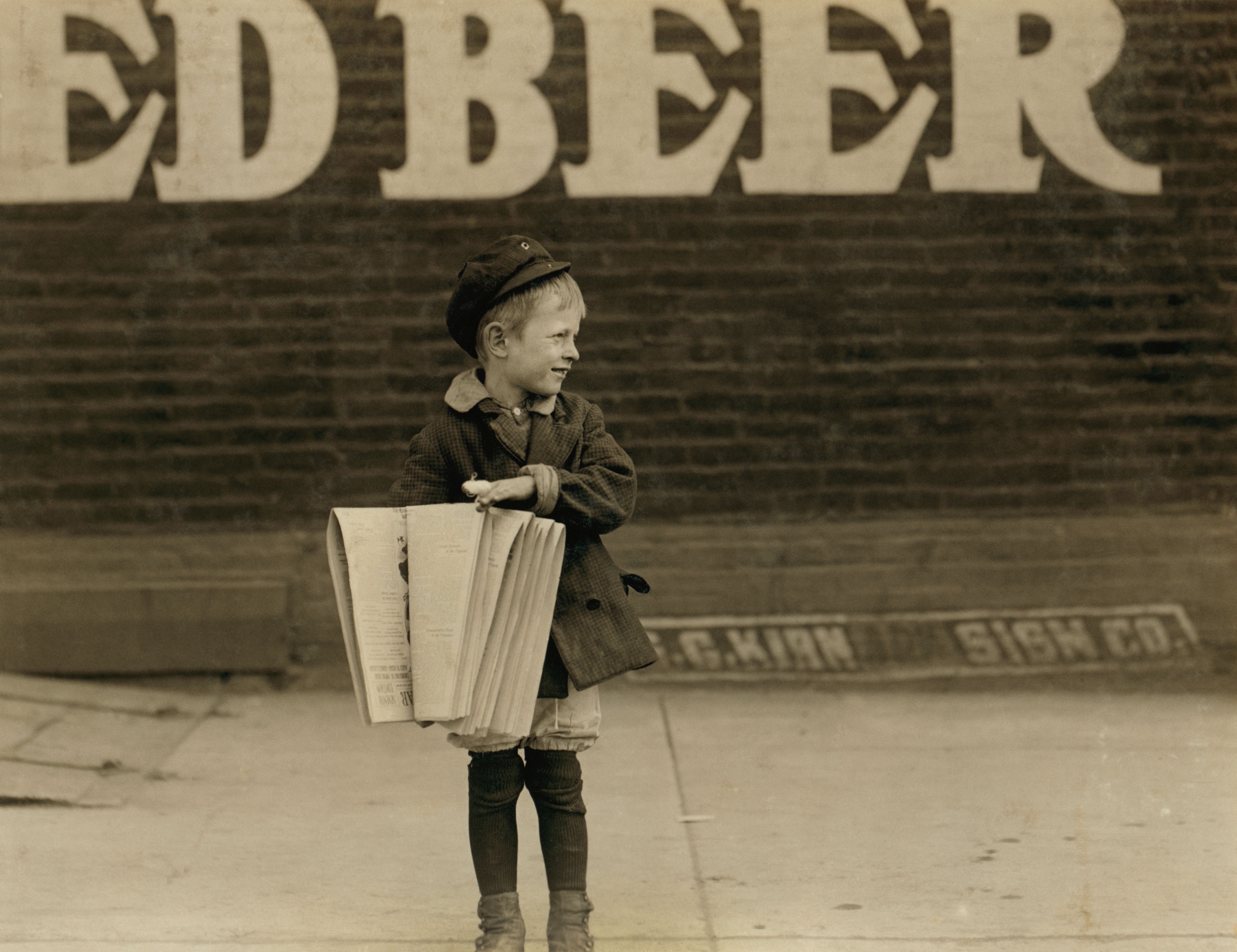 A newsie standing on a street corner in the early 20th century.