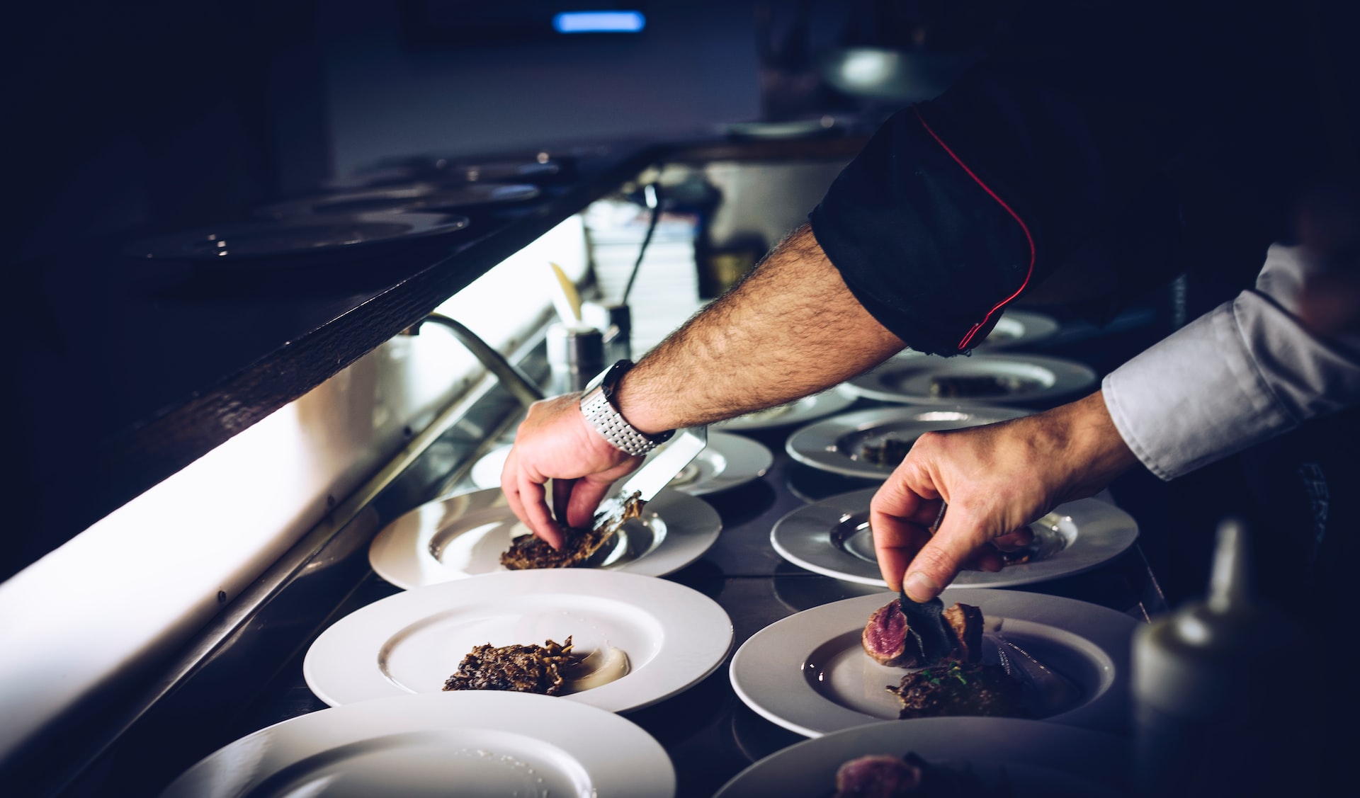 The hands of a restaurant worker plating dishes in the kitchen