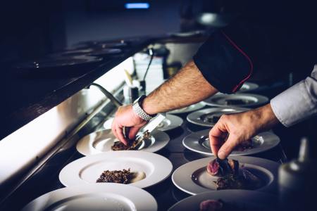 The hands of a restaurant worker plating dishes in the kitchen