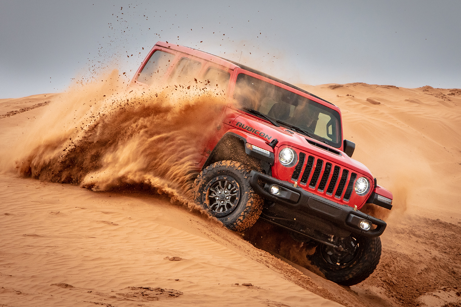 A red Jeep Wrangler Rubicon 392, powered by a V8 engine, driving through sand dunes