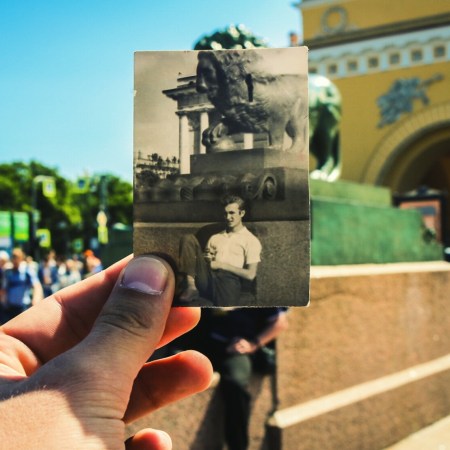 A man holding a photograph up in front of the same scene in present day.