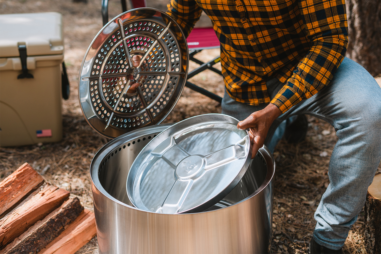 A man pulling out the removable ash pan from the Solo Stove Fire Pit 2.0, which was just released in August 2022