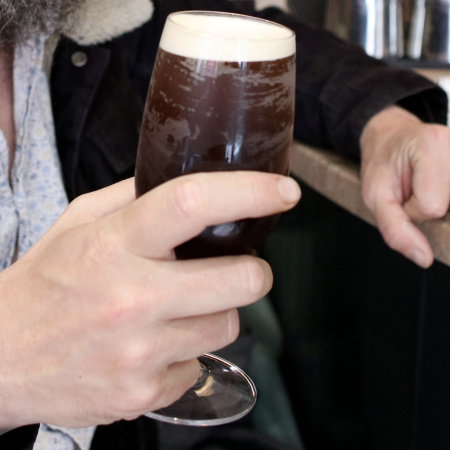 A man holding a frosty dark beer in a glass. Is this the summer of the tropical stout?