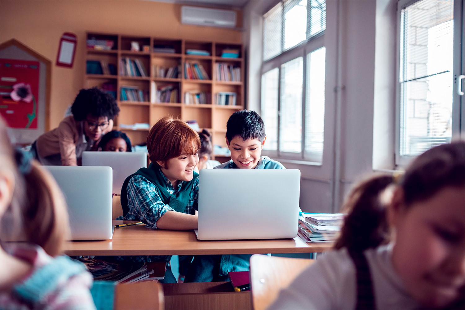 Two students in a classroom look at a laptop on a table