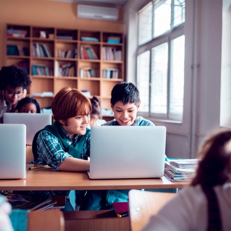 Two students in a classroom look at a laptop on a table