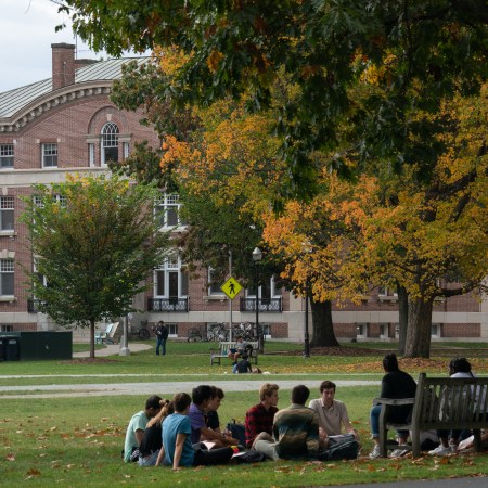 A group of students enjoy class outdoors under a tree on the Dartmouth University campus.