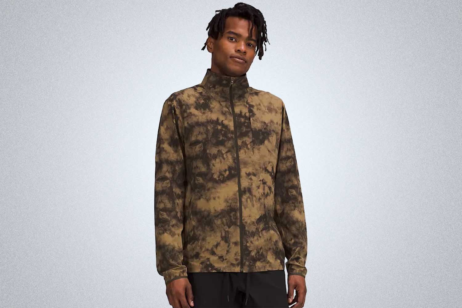 a model wearing a brown tie-dye zip jacket on a grey background