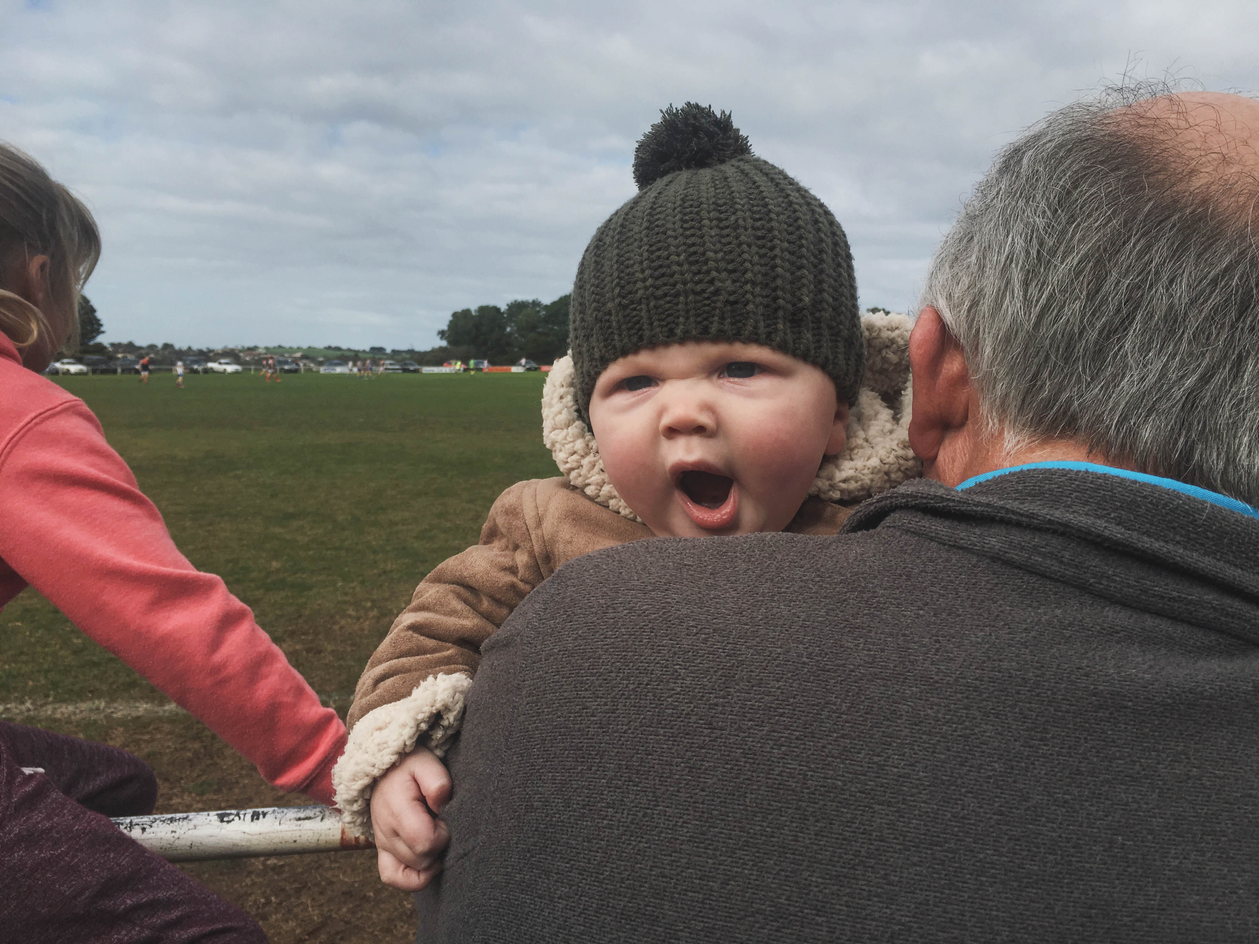 A baby yawning into the shoulder of an old man.